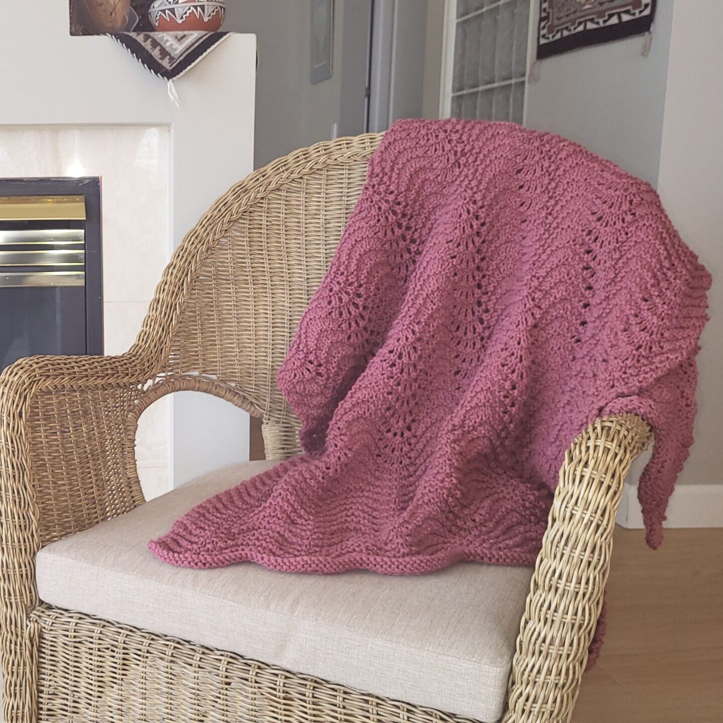 A pink knitted blanket thrown over a tan wicker chair