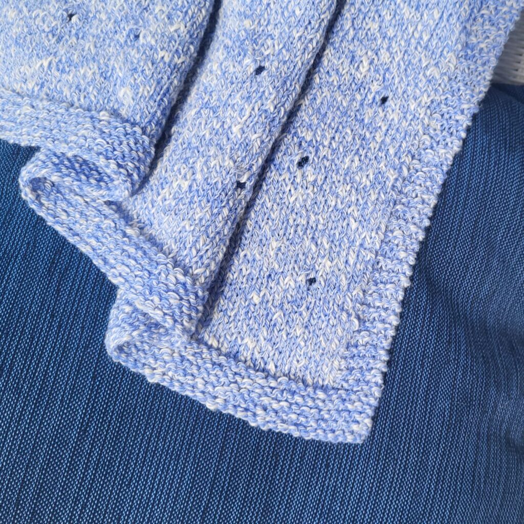 A blue knitted blanket on a dark blue pillow